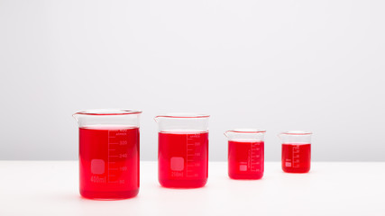 Four laboratory beakers with colored liquid over white background 
