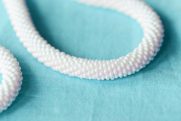 White beaded necklace on a blue textile background close up