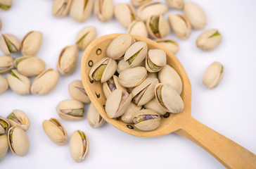 Oblong green pistachios in the wood spoon on a white background. Nutritious snack. Nuts filled with vitamins and minerals                          
