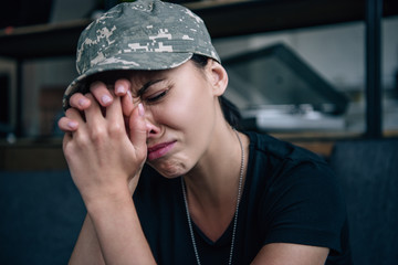 depressed woman in military uniform with clenched hands crying at home