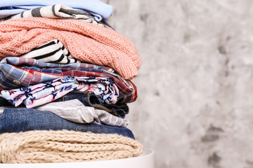 Stack of clean freshly laundered, neatly folded women's clothes on table. Pile of shirts, dresses and sweaters on white board, concrete wall background. Copy space, close up, top view.