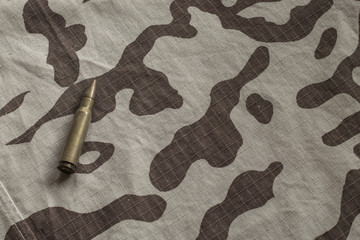 Bullet on camouflage fabric. Hunting cartridge on a military uniform. Desert camouflage with a...