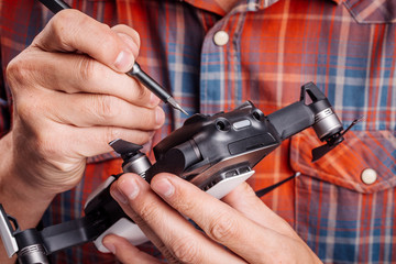 Man repairing quadcopter drone on table with different tools in modern workshop.