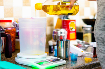 Yellow and white oil being poured into transparent container on weighing scale for soap making