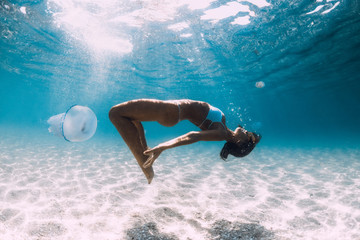 Woman diver glides over sandy sea with jellyfish. Freediving in blue ocean