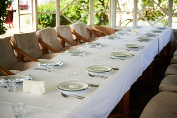 Served long white table with plates and cutlery. Preparing for the banquet, celebration.