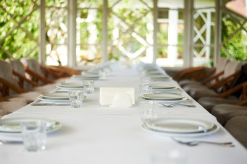 Served long white table with plates and cutlery. Preparing for the banquet, celebration.