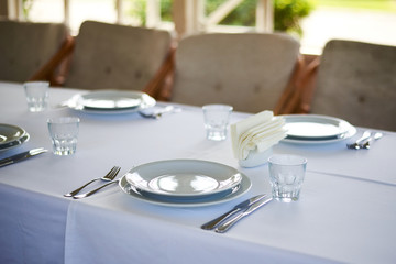 Served long white table with plates and cutlery. Preparing for the banquet, celebration.