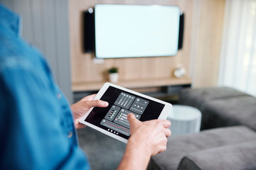 Hands of young man holding tablet with smart remote control system