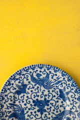 Blue Dragon Chinese China Plate set on a bright yellow table top. Still Life Photography.