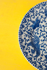 Blue Dragon Chinese China Plate set on a bright yellow table top. Still Life Photography.