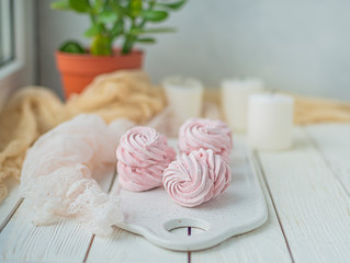 Obraz na płótnie Canvas homemade Marshmallow zephyr on a white plate with candles and room tree on a light wooden table. Pink sweet homemade marshmallow. Colorful meringues on a white background. dessert