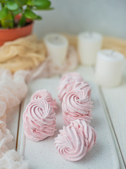 homemade Marshmallow zephyr on a white plate with candles and room tree on a light wooden table. Pink sweet homemade marshmallow. Colorful meringues on a white background. dessert