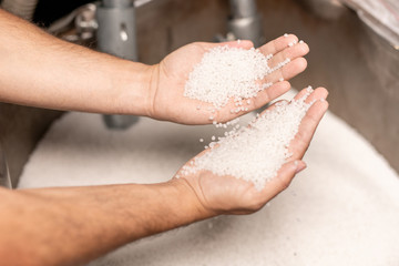 Human hands holding two piles of white polymer granules