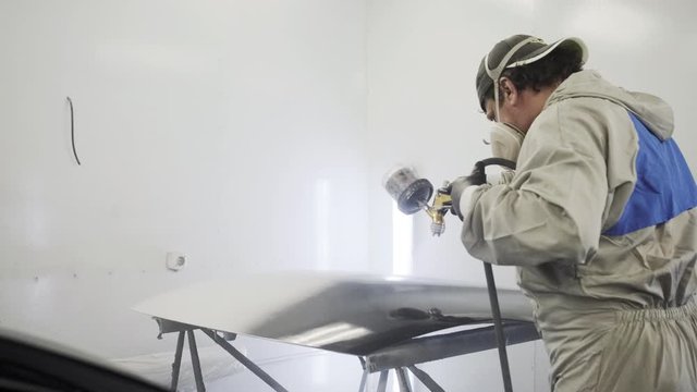 Painter is working in paint-spraying booth of car service, coloring auto detail