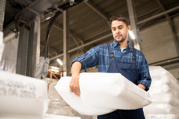 Young man in workwear carrying heavy white sack with polymer granules