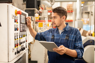 Young engineer checking data on control panel while setting working parameters