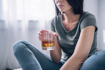 Cropped view of depressed woman with whiskey glass at home