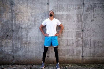 Fit and attractive sportsmen against concrete wall background listening to music and looking up. Motivational preparation before training.