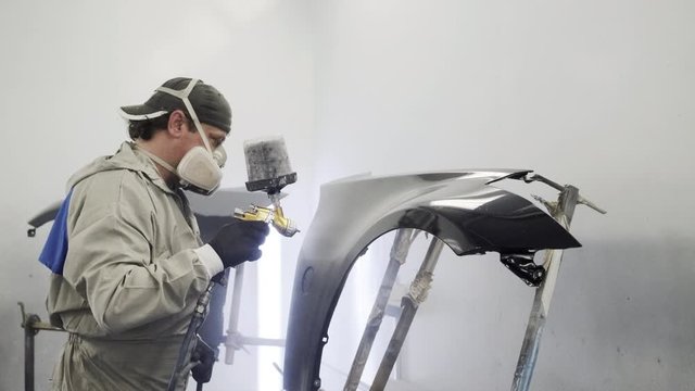 Male specialist is dyeing metal detail of car body inside paint-spraying booth,