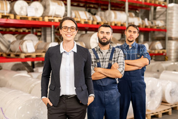 Happy young elegant female leader of engineering team and two men in workwear