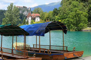 Lake Bled with traditional boats. Beautiful mountain lake in summer with small Church on island with castle on cliff and alps in the background.