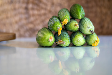 on the kitchen table are several freshly picked green cucumbers, in the background a wicker basket