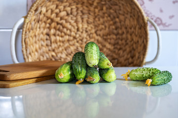 on the kitchen table, freshly picked green cucumbers and a wooden cutting board, in the background a straw wicker basket, close-up, horizontal frame, copy space