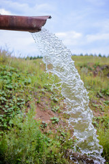 The flow of water pours out of the pipe in the countryside
