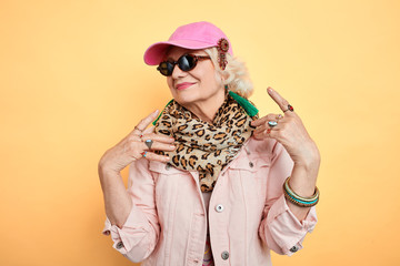cool granny in stylish street clothes posing to the camera. isolated yellow background. studio...
