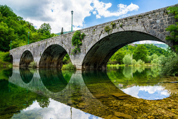 Montenegro, Beautiful ancient stone bridge over river crnojevica near town cetinje in skadar lake national park reflecting in silent glassy water