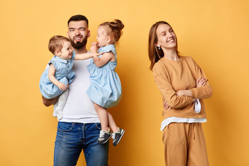 best help from husband, unforgettable Mother's day.unhappy depressed male babysitter cannot cope with his duty. carefree wife with crossed arms looking away. isolated yellow background, studio shot - obrazy, fototapety, plakaty
