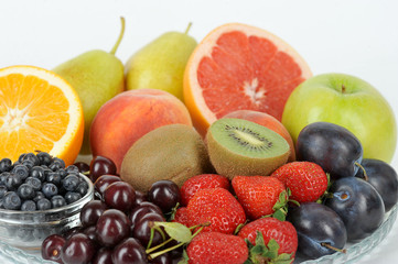 In a plate are orange, grapefruit, cherry, plum, pears, peaches, apple, plum, blueberries, kiwi. Light background. Close-up. Macro shot.