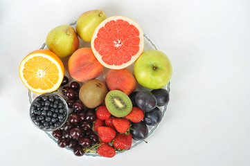 Acceptable fruits for diabetes. In a plate are orange, grapefruit, cherry, plum, pears, peaches, apple, plum, blueberries, kiwi. View from above. White background. Free space for text.