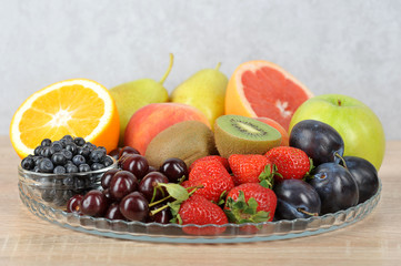 In a plate are orange, grapefruit, cherry, plum, pears, peaches, apple, plum, blueberries, kiwi. Light background. Close-up. Macro shot.