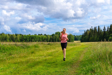 young woman jogging in the meadow and listening to music on headphones