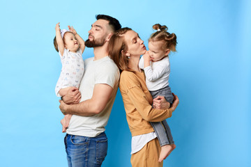 two caring parents standing back to back and holding their children in arms. close up photo. isolated blue background. studio shot. - 282319098