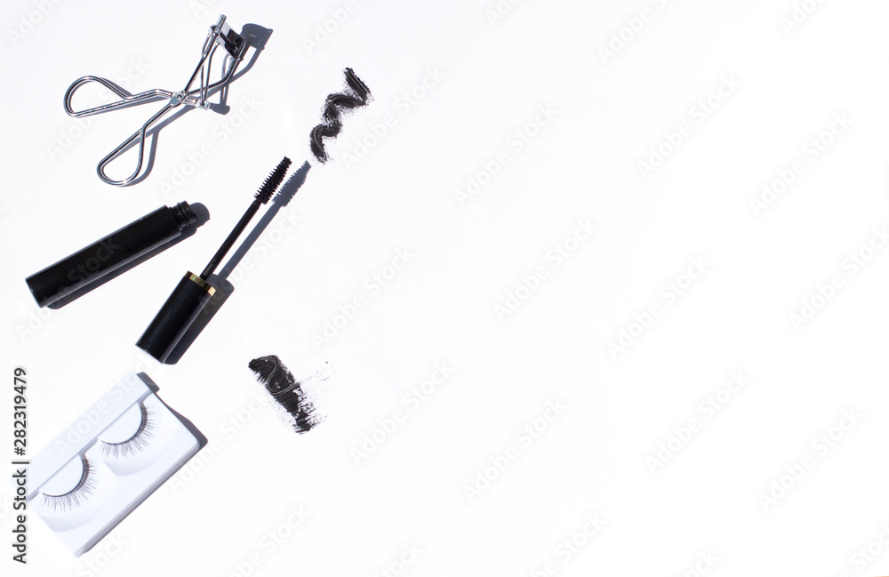 Wall mural Black mascara frame with brush smear, an eyelash curler and false eyelashes on the white background. Cosmetic isolated products. Copy space