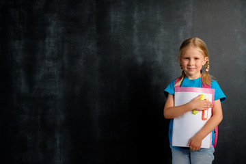 Schoolgirl with a briefcase on the background of a school board for chalk. Back to school concept with copy space.