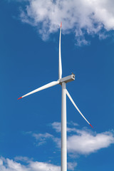 A wind turbine and blue sky with clouds. Large three-bladed horizontal-axis wind turbines produce...