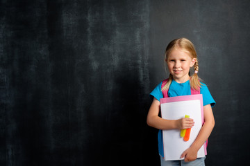 Schoolgirl with a briefcase on the background of a school board for chalk. Back to school concept with copy space.