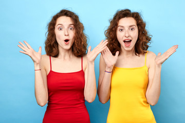 Close-up portrait of young emotional surprised two women with opened mouth standing with open palms, isolated on blue background. Oh. my God. emotion and feeling