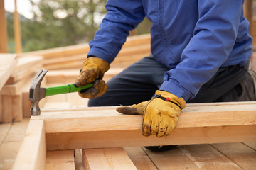 Male builder in yellow gloves hammer nail into wooden structure. Construction concept