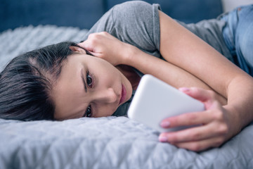 lonely sad woman on bed using smartphone in bedroom