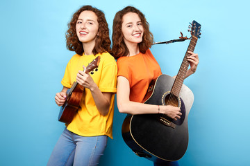 cheerful beautiful sisters are interested in music. women playing rock music. isolated blue...