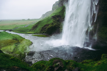Cold pale white water of Seljalandsfoss  waterfall in Iceland. Typical windy weather.