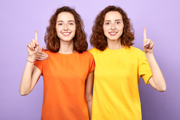 Happy beautiful twins girls point up isolated on blue background, two sisters showing something above their heads , advertisement, place for text, body language