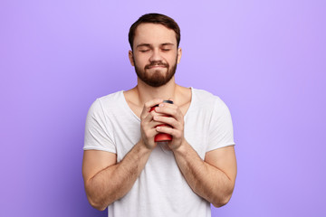 happy handsome man with closed eyes holding hot morning coffee. guy enjoying drinking takeaway coffee. time for coffee break, free time, spare time, lifestyle