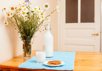 Simply stylish wooden kitchen with bottle of milk and glass on table, summer flowers camomile, healthy foog moring concept close up