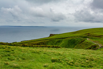 Seascape and a rural trail between the Irish countryside of the coastal route walk from Doolin to the Cliffs of Moher, geosites and geopark, Wild Atlantic Way, cloudy day in county Clare in Ireland